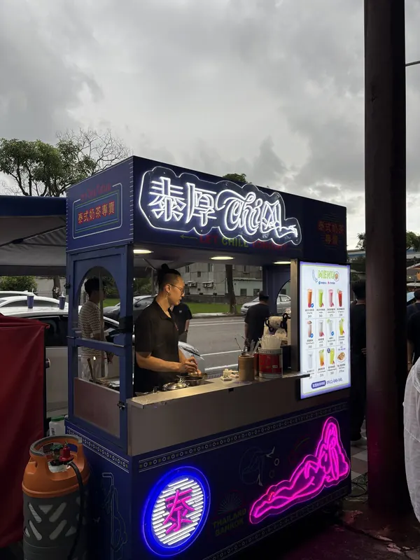 傍晚的活動會場,泰厚 CHILL 攤車亮著霓虹招牌與菜單燈箱,夥伴在攤位裡製作飲品