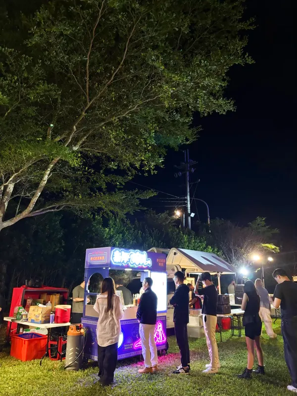 夜裡樹下,賓客在亮著霓虹招牌的攤車前排隊拿飲料