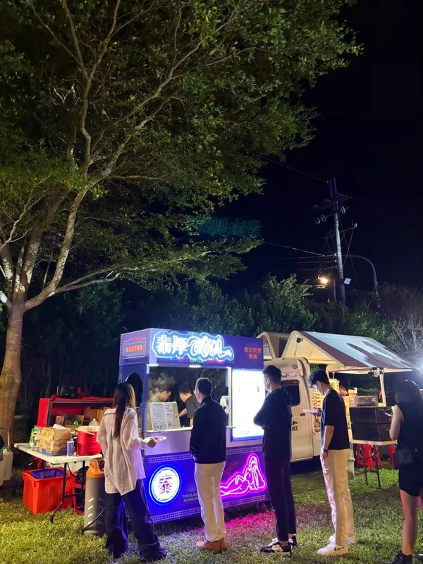 樹下的攤車與排隊的賓客,遠處路燈與帳篷