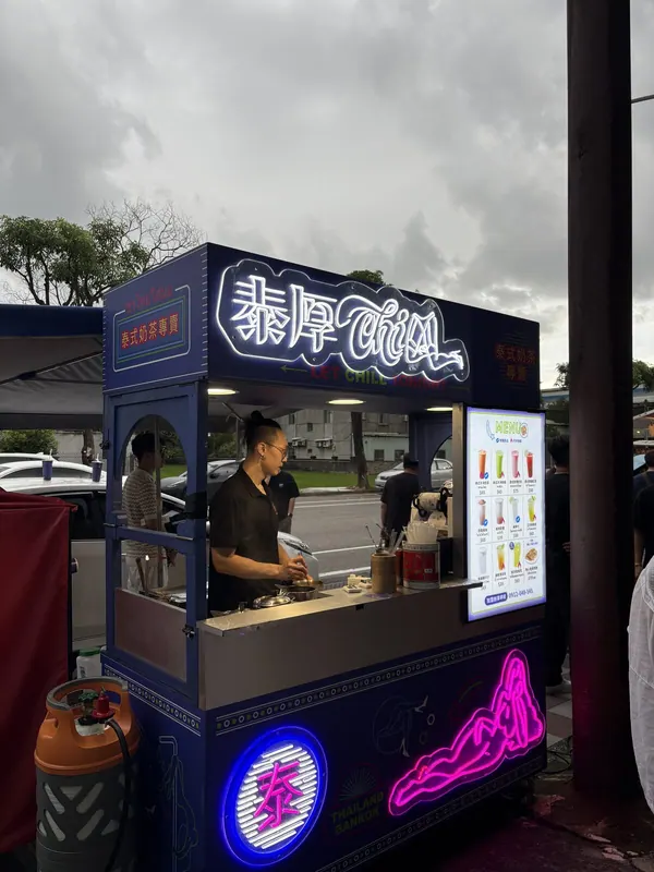 桃園戶外會場的雨棚下,亮著霓虹招牌的泰厚 CHILL 攤車,夥伴正在製作飲料(憑券或現點)