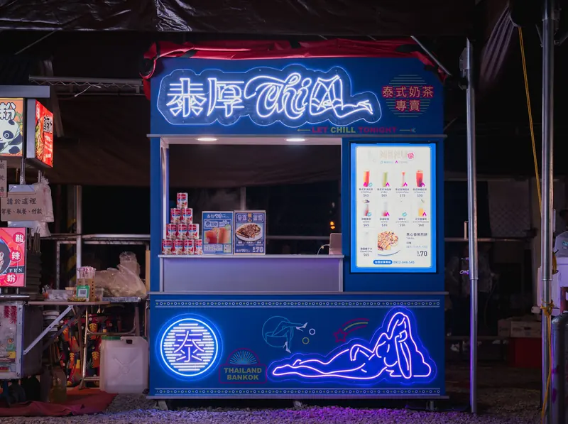 夜裡亮著霓虹招牌的泰厚 CHILL 攤車,側面是粉紅霓虹女子與藍光泰字章