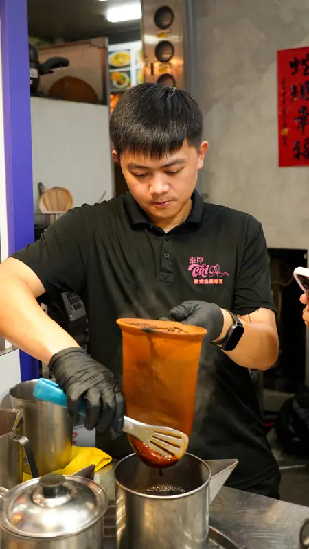 店員戴著手套,把布袋沖濾好的橘紅色泰式奶茶倒進杯中