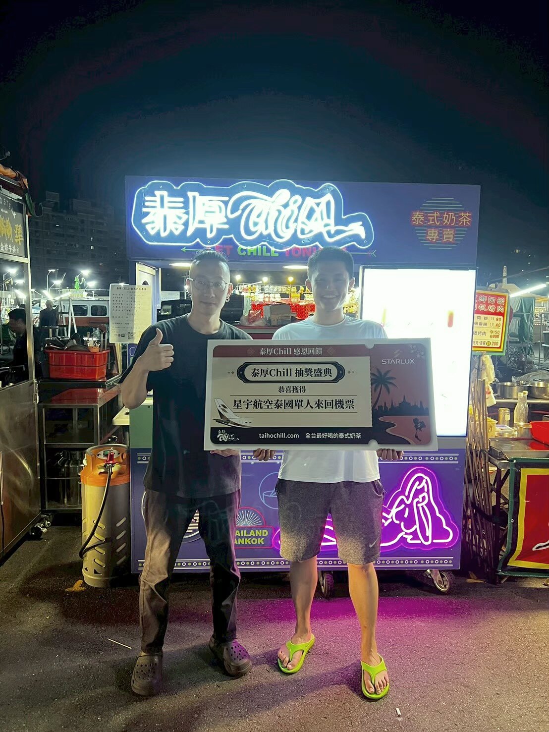 大慶夜市旗艦店霓虹招牌下，得主與店員手持星宇航空泰國機票獎牌合影